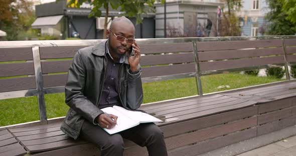 Young Black Man Sitting on a Bench with a Phone