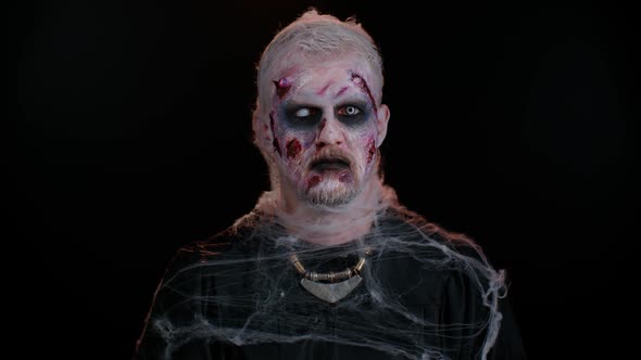 Sinister Man with Horrible Scary Halloween Dead Zombie Makeup in Costume Looking Ominous at Camera