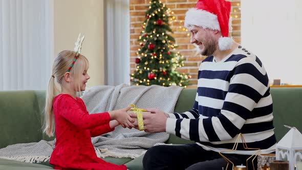 Father gives a Christmas gift to his daughter dressed in festive red dress