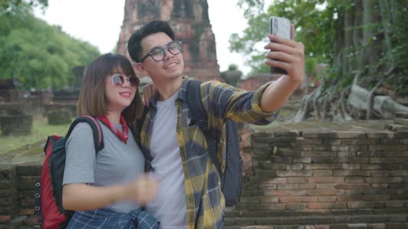 Asian couple using smartphone taking selfie while spending holiday trip at Ayutthaya, Thailand