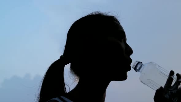 Silhouette of woman drink of water in slow motion at sunset 