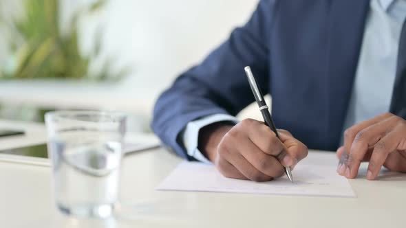Close Up of Hands of African Businessman Writing on Paper