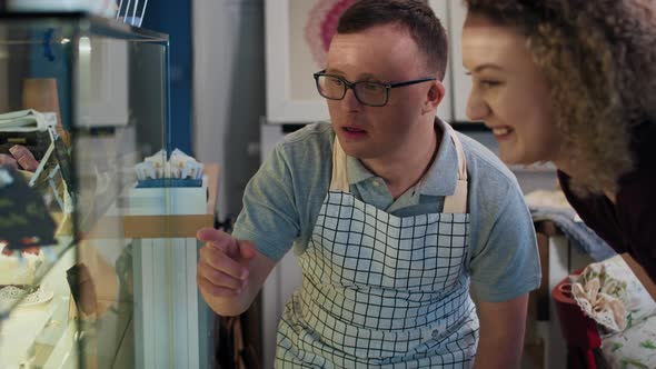 Caucasian waiter with down syndrome advising client a dessert from the fridge in a cafe. Shot with R