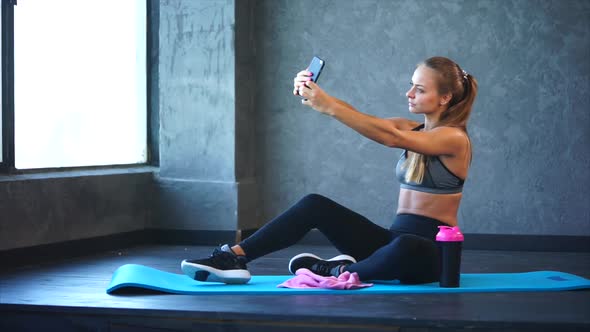 A Young Girl with a Good Figure Makes Selfie on a Mobile Phone in the Gym