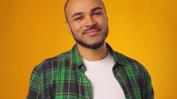 Young African American Man in Casual Shirt Smiling and Raising Eyebrows Against Yellow Background