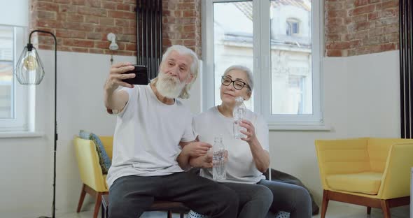 Old Couple Clinking Bottles with Water while Having Video Call with Friends