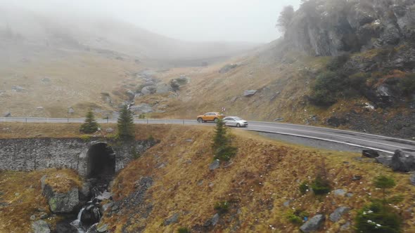 Aerial Shot of Orange Car Riding Through Mountain Road at Autumn