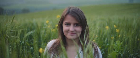 A young woman in a middle of a green wheat field, smiling, feeling happy. 