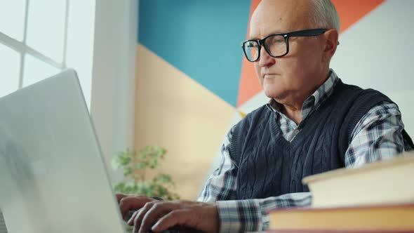 Slow Motion of Retired Man Using Laptop Computer Typing at Desk in Apartment