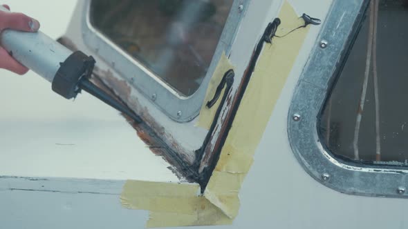 Carpenter using sealant gun to repair leak on wooden boat. MEDIUM SHOT