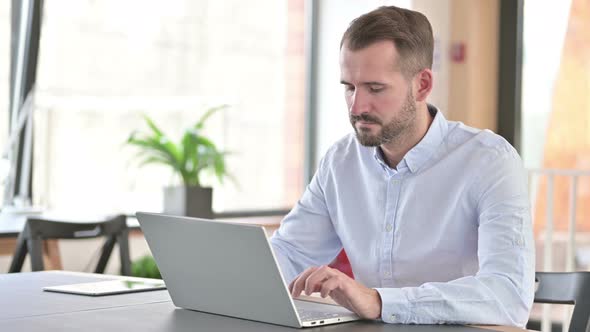 Young Man with Laptop Smiling at Camera in Office 