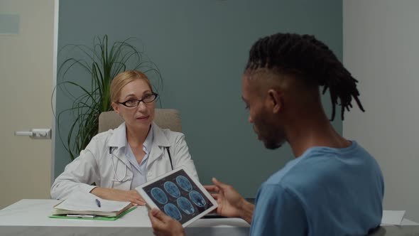 Patient Looking at MRI Digital Image on Tablet Asking Doctor Indoors