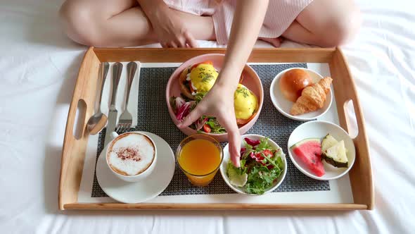 Woman Eating Breakfast in Bed in Cozy Hotel Room