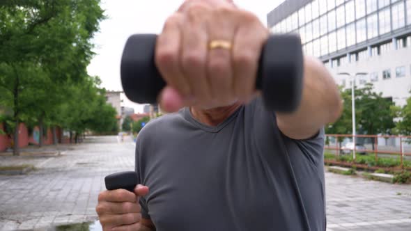 Senior man boxing with dumbbells during training in city