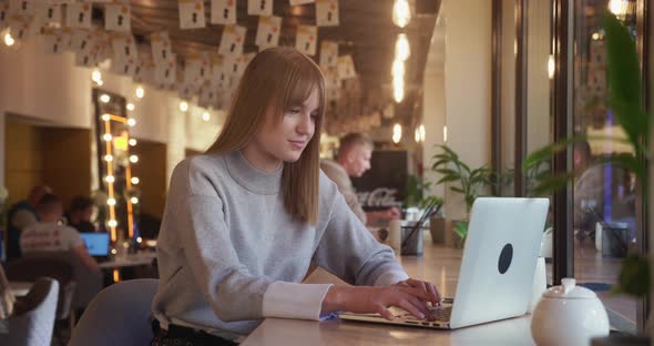 Cute Blonde Woman Typing Message in Laptop Sitting in Cafe