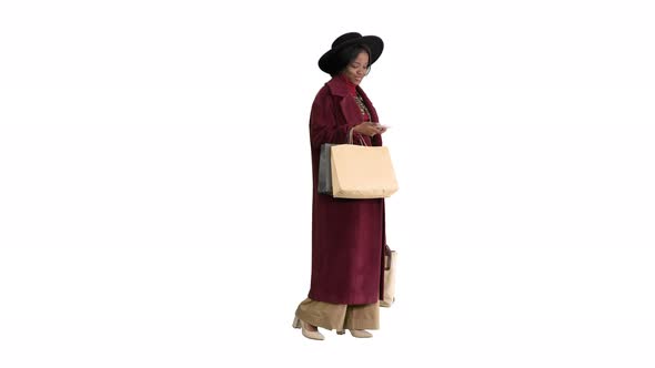Smiling African American Fashion Girl in Coat and Black Hat Texting on Her Phone on White Background