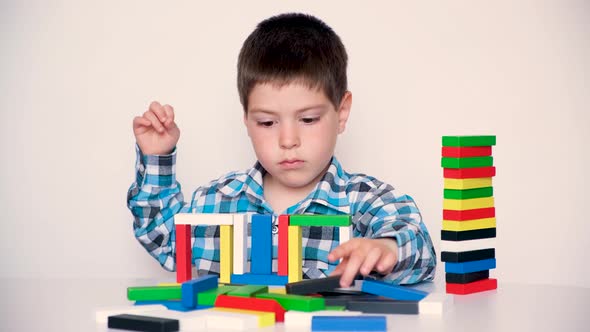 A 4Yearold Boy Plays with Multicolored Wooden Blocks Builds Towers on a White Background