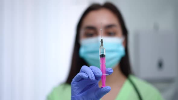 Syringe with Coronavirus Vaccine in Hand of Blurred Female Doctor in Covid19 Face Mask