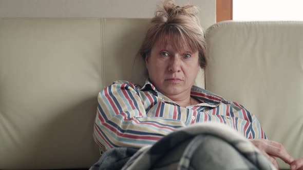 Emotional senior caucasian woman sits on the white sofa at home in front of the TV