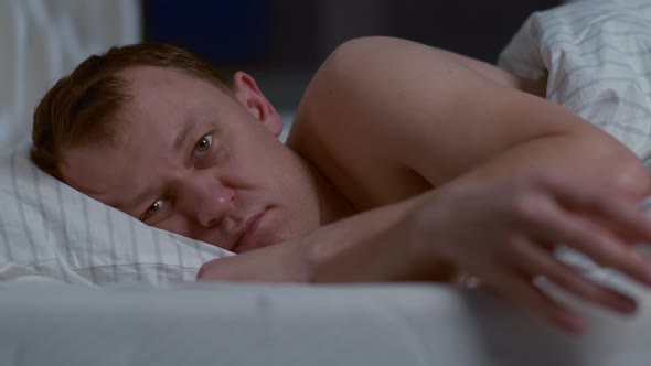 Attractive man lying in bed at night cannot sleep, insomnia