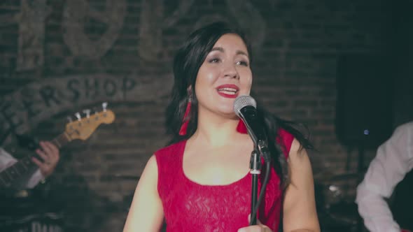 Young Attractive Girl Singing Into Microphone on Stage with Musicians