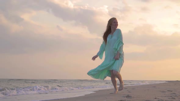 The Young Red-haired Smiling Girl Run in the Green Dress at Beach By the Sea in Summer