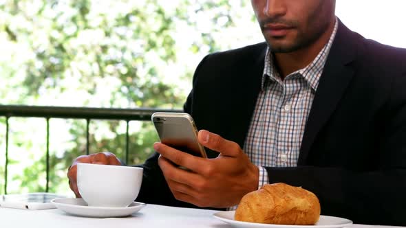 Businessman using mobile phone while having breakfast