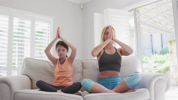 Mother and daughter practicing yoga while sitting on the couch at home