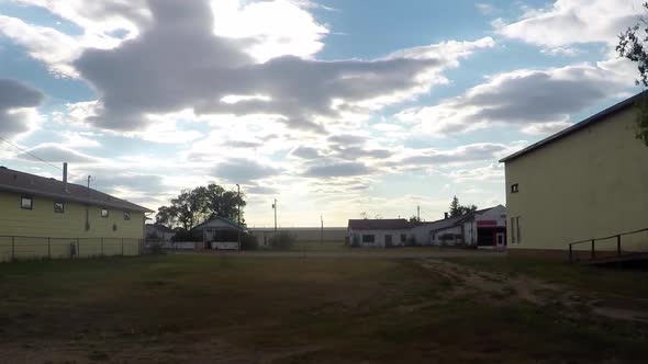 TIME LAPSE - Slow zoom out of of a street in a small town and a couple buildings.  Clouds travel fas