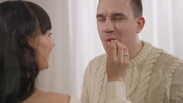 Closeup of Satisfied Brunette Caucasian Man and Woman Feeding Husband with Sweet Tasty Candies