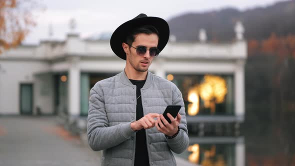 A Man is Standing on the Quay and Texting on a Smartphone