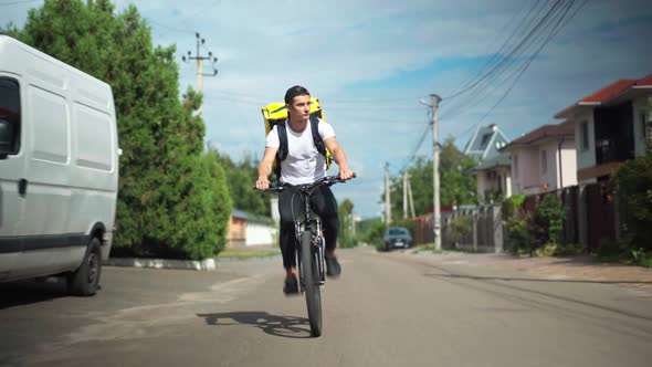 Wide Shot Front View Confident Delivery Boy Driving Bicycle Fast on Sunny Street in Town