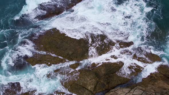 Aerial view top down of big waves crashing on rocks in dark blue ocean. Beautiful sea waves water