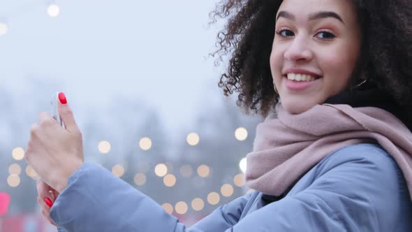 Smiling Afro American Woman Stands Outdoors in Winter Looking at Camera Smiling Takes Pictures on