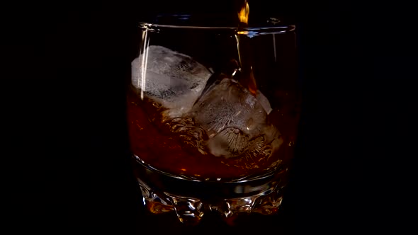 Pouring whiskey into a glass with ice on an isolated black background. Slow motion.