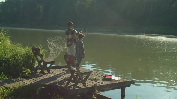 Multiethnic Family with Son Fishing with Rod on Wooden Pier By Lake at Sunrise