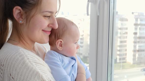 Portrait of Smiling Mother with Little Baby Son Looking on City Street Through Window