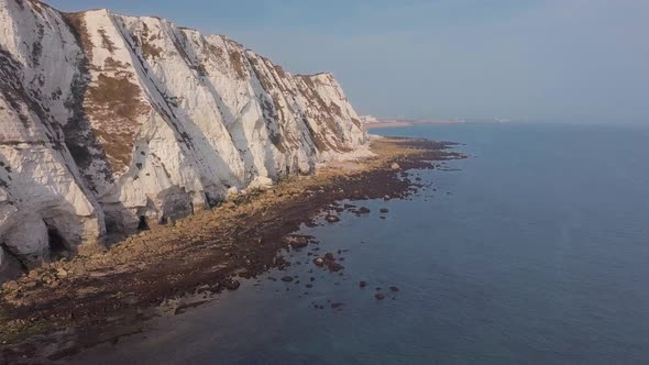 Drone flies low towards the White Cliffs of Dover with camera panning up. Beautiful turquoise sea in