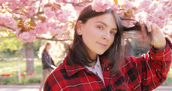 Portrait of beautiful European young woman in red jacket with pink cherry blossoms background