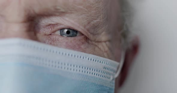 Macro Face Part of Blue-eyed Senior Man in Mask Looking at Camera on Background