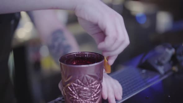 Unrecognizable Young Bartender Rubs a Clay Glass of Cocktail with the Orange Peel Before Serving