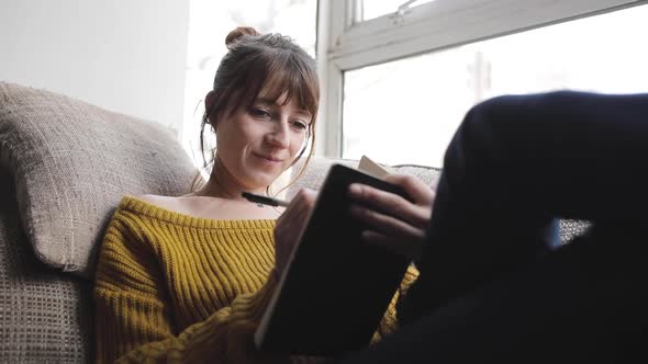 Slow motion shot of woman sitting on couch and writing into a book