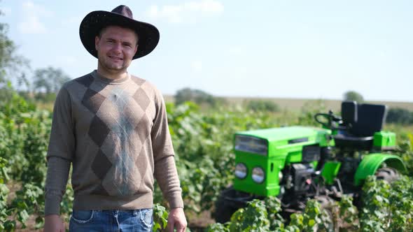 A Proud Young Farmer Stands in Front of His Green Tractor