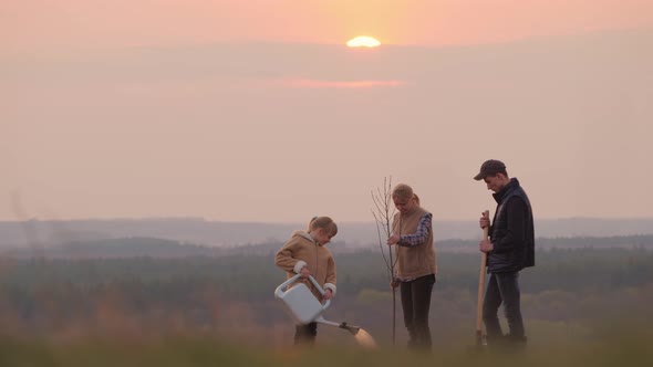 Family with a Tree Seedling, a Sprinkler and a Shovel Standing in a Picturesque Place