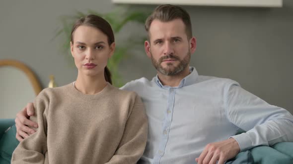 Portrait of Couple Looking at Camera While Sitting on Sofa