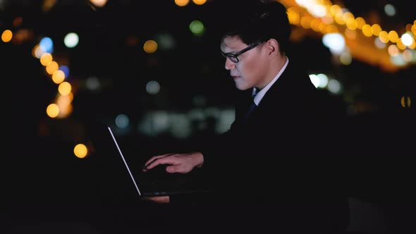 Business man use laptop on rooftop of high building at night in the big city with traffic lighting