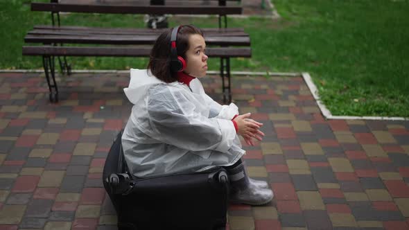 Side View Relaxed Little Woman in Rain Coat and Headphones Listening to Music Smiling Sitting in