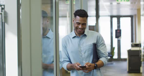 Video of happy biracial businessman using smartphone in office