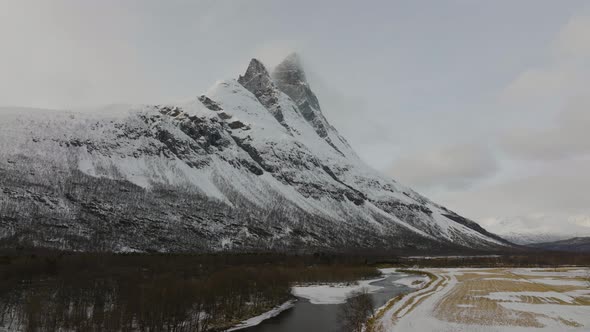 Flying over the forest and river towards the snow covered Otertinden mountain summit in northern Nor