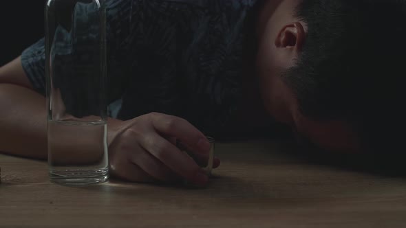 Drunk Asian Man Pouring Vodka In A Shot Glass Before Drinking And Sleeping In Black Background